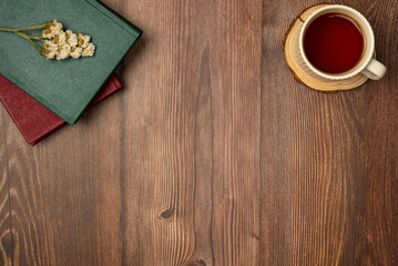 Books with cup of tea on wooden background from above. Flat lay, top view. Copy space
