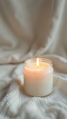 A burning candle decor on a white knitted fabric. Atmospheric, romantic mood, relaxation