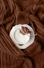 Mocha Mousse - color of the year 2025. cup of cappuccino coffee on sweater top view flat lay