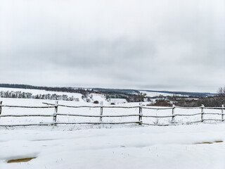 A snow covered field with a white fence in the foreground