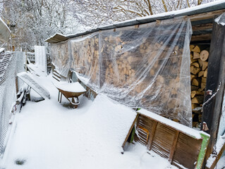 A pile of wood is covered in snow next to a shed