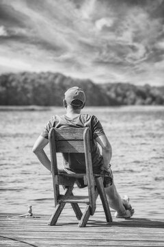 A man sits on a boat dock by the lake and enjoys the beautiful, idyllic nature in summer.