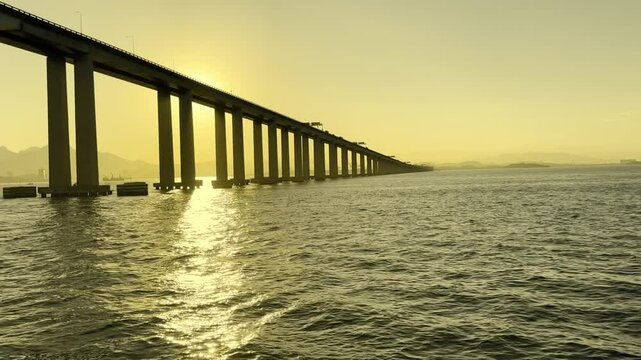 Take passando por baixo da ponte Rio - Niter&oacute;i pela Ba&iacute;a de Guanabara em um lindo por do sol com c&eacute;u limpo e amarelado.