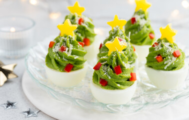 Festive stuffed eggs christmas trees on a plate decorated with red and yellow bell peppers and parmesan. New Year's snack, symbol. Close up. Selective focus