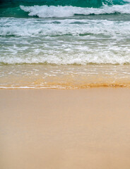 A sandy beach on the coastline of the ocean with clear water with small waves.
