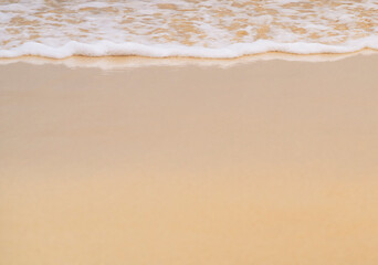 Clean sandy beach by the ocean, small waves with foam washing the shore, close-up view of golden yellow sand from copy space.