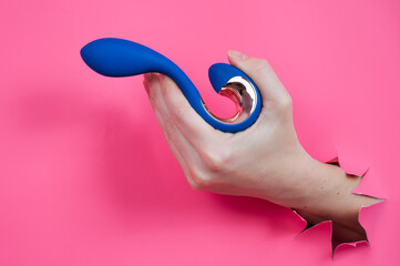 Hand with blue vibrator sticking out through pink paper background. 