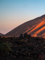 A volcanic landscape with black lava formations and a mountain in the sun.