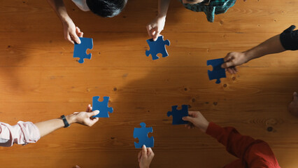 Top down view of skilled business people separated blue jigsaw puzzle on meeting table. Group of...