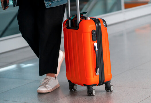 Red suitcase, a person with a travel bag at the airport.