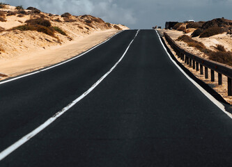 An asphalt road among desert with sandy dunes.