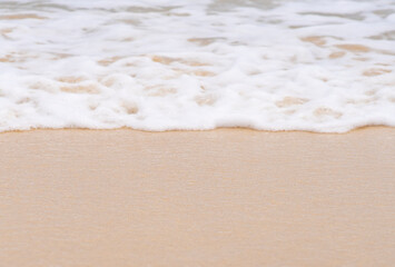 Clean sandy beach by the ocean, small waves with foam washing the shore, close-up view of golden yellow sand from copy space.