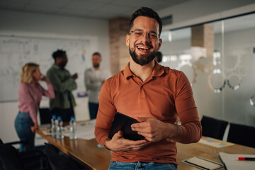 Smiling businessman holding tablet and leading meeting in modern office