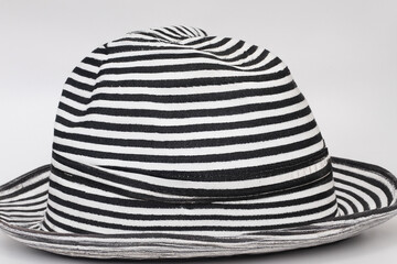 Black and white striped hat with black band. Summer hat with gray background. Woman lies on gray hat with a striped background. A woman lies in a hat on a gray striped background in lifestyle summer.