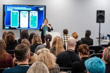 Diverse group of individuals attending a presentation about innovative technology solutions, engaging with speaker and digital display. Setting represents modern education and professional growth.