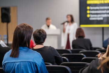 Diverse group attending educational seminar, focused on speakers' presentation. Engaged atmosphere in conference room.