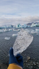 Laguna rzeki lodowcowej Jokulsarlon. Południowa Islandia lodowiec Vatnajökull. Kawałek lodu z lodowca w dłoni w rękawiczce na tle islandzkiej laguny lodowcowej.  © onlytraveler