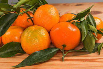 Heap of clementines on twigs with leaves on wooden surface