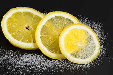 Sliced lemons on black background. Black background with sugar and lemons. Black background with slices of lemon and sugar lying on a plate. A lemon and a slice of sugar lies on a black lifestyle.