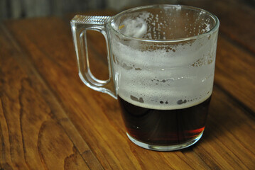 glass of beer on wooden table. Beer foam on the walls of a glass of dark beer