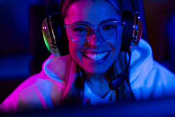 Photo of cute charming blonde girl look monitor cheerful smile play gamer computer purple blue neon light indoors late night