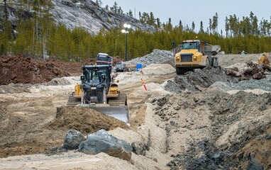 Bulldozer spreading sand with a dump truck circulating in the background