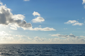 Fototapeta premium The sun shines brightly over the ocean in this photo. Clouds and sea in the sky. A sea blue sky with a sun glare. A blue sky with clouds and blue clouds glares at the sea sun lifestyle.