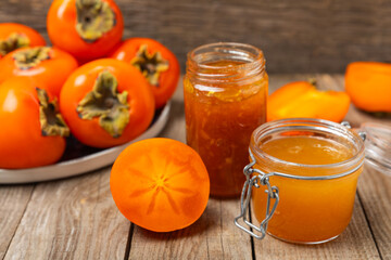 Persimmon jam with slices of ripe persimmon on wooden textured table. Delicious persimmon jam. Marmalade. Healthy sweets. Vegan. Close-up. Space for text. Copy space.