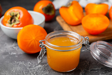 Persimmon jam with slices of ripe persimmon on wooden textured table. Delicious persimmon jam. Marmalade. Healthy sweets. Vegan. Close-up. Space for text. Copy space.