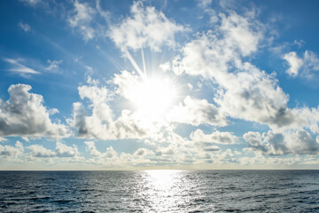 Obraz premium The sun shines brightly over the ocean in this photo. Clouds and sea in the sky. A sea blue sky with a sun glare. A blue sky with clouds and blue clouds glares at lifestyle the sea sun.