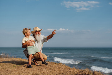 Grandfather teaching his grandson about the world, pointing at the ocean horizon on a sunny day, sharing a moment of wisdom and bonding during their time at the beach