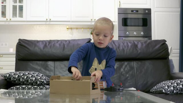 Impatient child unboxing new toy at home. Excited little boy unpacks remote-controlled transformer car.
