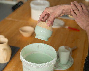 Close-up of a potter's hands glazing a pottery piece. 