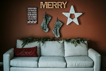 White couch against an orange wall with Holiday Decorations. Stockings, a star and the word Merry.