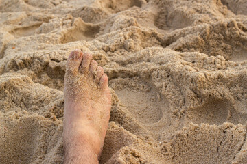 A close-up view of a foot resting on the beach, relaxing in the warm sand.