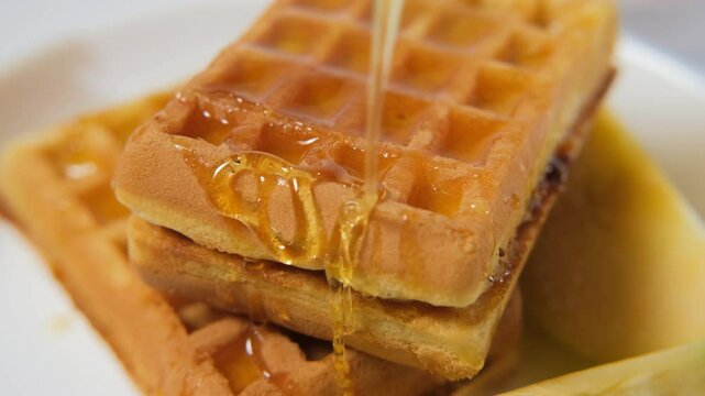 Close-up of hand pouring golden honey on stack of waffles and slices of apples, delightful breakfast, slow motion