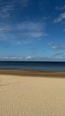Serene sandy beach meets the calm blue sea under a vibrant sky, creating a balanced 50/50 effect between sand and sky, perfect for tranquility and inspiration