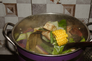 Sayur asem is full of fresh, hot vegetables that have just been cooked and removed using a spatula from a coconut shell.