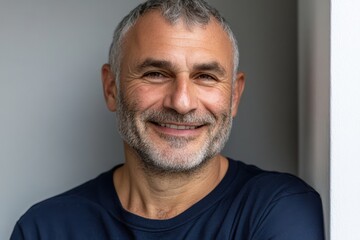 Fototapeta premium A friendly middle-aged man with salt-and-pepper hair shares a warm, welcoming smile in a relaxed setting.