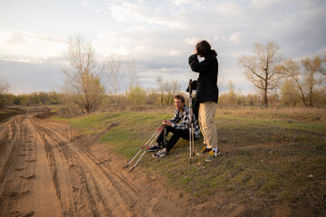 Two men engage in conversation while hiking on a sandy path surrounded by trees during a beautiful sunset