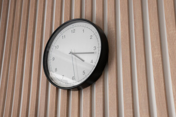 A wall clock with a black frame and white face hangs prominently on a wooden striped wall, indicating the current time clearly