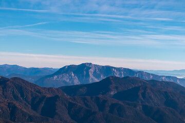 Fototapeta premium Majestic mountain peak Dobratsch seen from top of mount Piper in Julian Alps, Friuli Venezia Giulia, Italy. Lush green rolling hills covered with forest in Carinthia, Austria. Wanderlust Val Canale