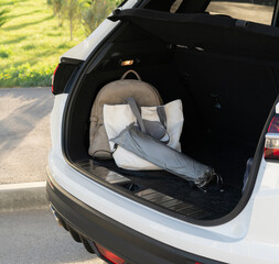 A car trunk is open, showing a backpack and an umbrella resting inside, set in a sunny parking lot...