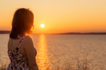 Woman standing in front of lake at sunset. Girl in blue sky at sunset. A sunset over the river and nature. A girl in a blue dress and blue skirt and a blue sky at lifestyle sunset in nature.
