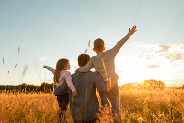 Father and his children walking in a field at sunset enjoying time together in nature, family future, single parent concept 