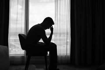 Sad man in a dark room full of desperation thoughts. Portrait of thoughtful sad man alone. Fear,...