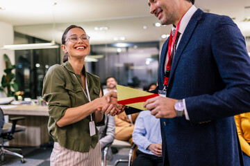 Front view of businesswoman receiving award from businessman in front of business professionals...