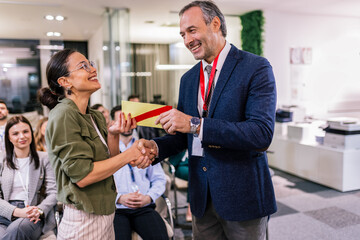 Front view of businesswoman receiving award from businessman in front of business professionals...