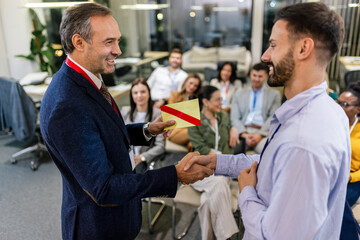 Front view of businessman receiving award from businessman in front of business professionals...