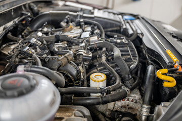 Close-up of a car engine, emphasizing various components, hoses, and an oil filter, in a workshop setting. Concept of automotive maintenance